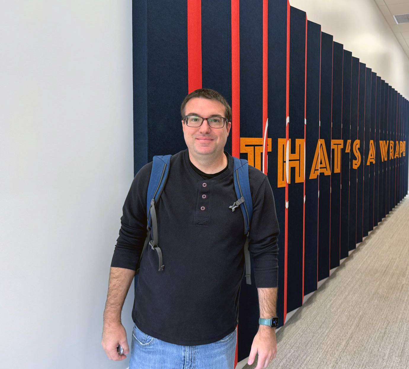 Gary standing in front of a colorful wall. On the wall are orange letters that spell out That's a Wrap